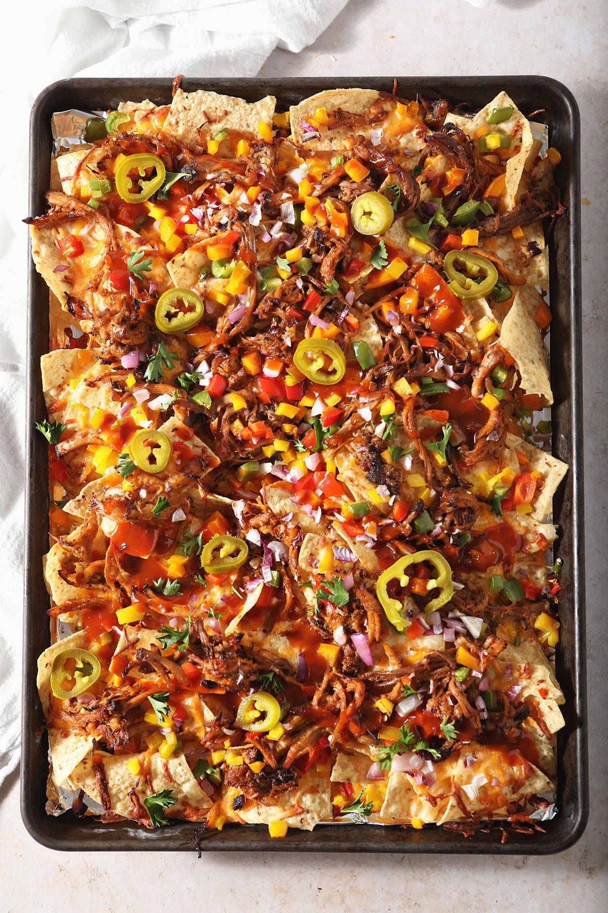 A tray exhibits loaded nachos adorned with shredded meat, melted cheese, jalapeños, diced tomatoes, and red onions on a light background.