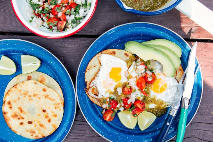 Eggs, salsa, and avocado on top of tortillas on blue camping plates.