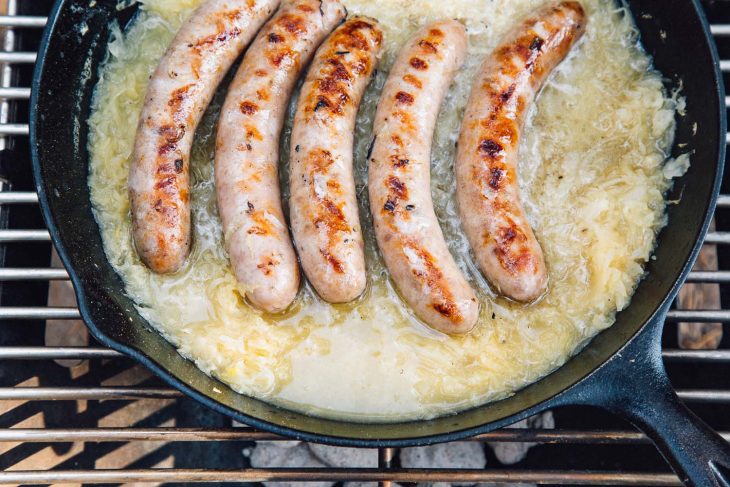 Beer brats simmering in beer and sauerkraut in a cast iron skillet