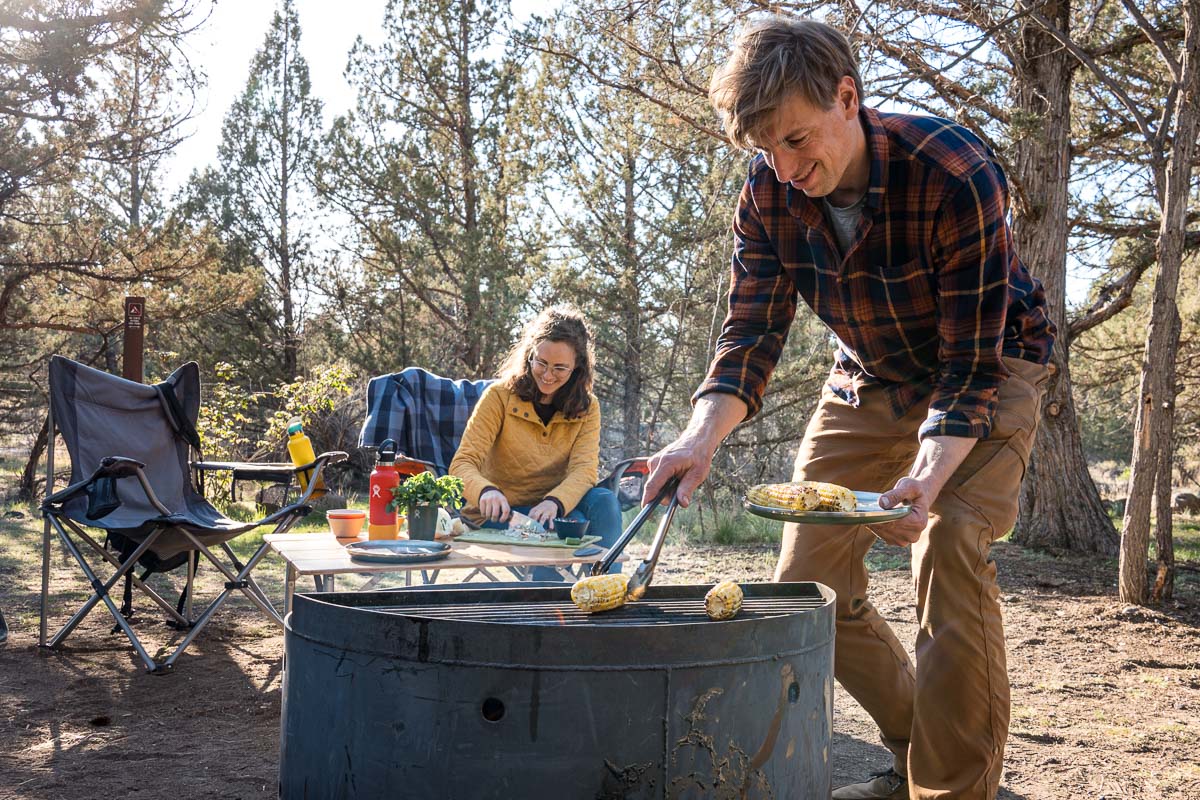 Michael placing corn on the cob over a campfire.