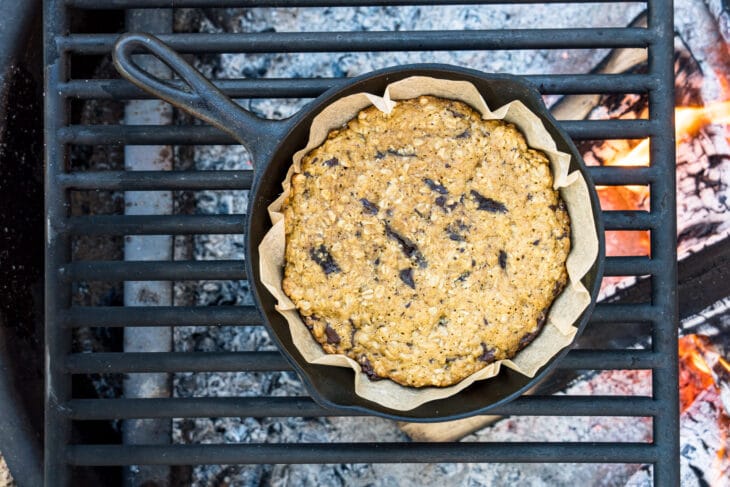 A chocolate chip cookie in a cast iron skillet over a campfire