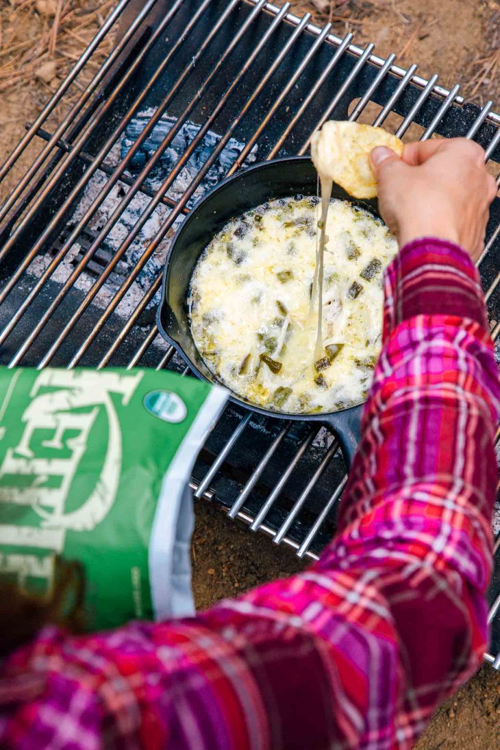 Dipping a chip into a skillet of queso fundido on a campfire.