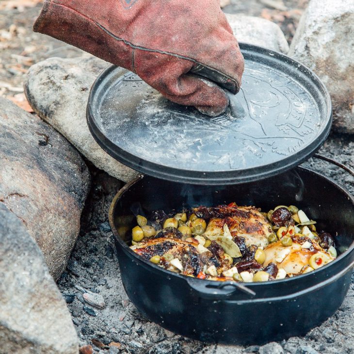 Michael lifting the lid off of a Dutch oven sitting in a fire pit.