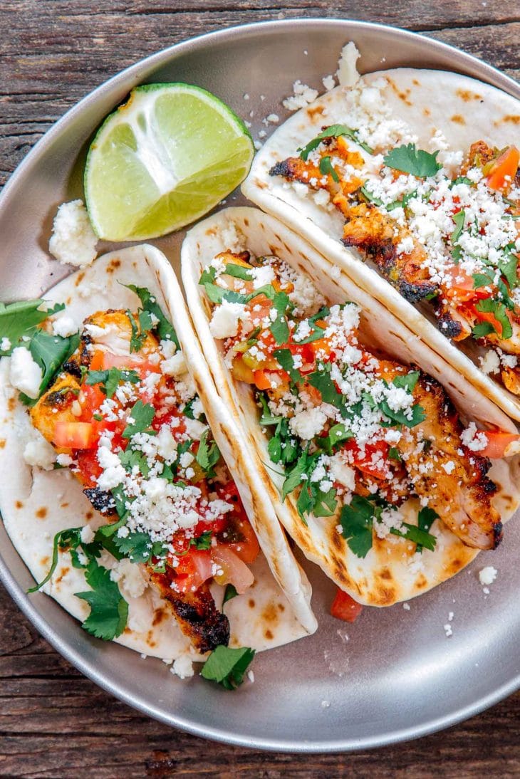 Three grilled chicken tacos on a plate with sliced limes