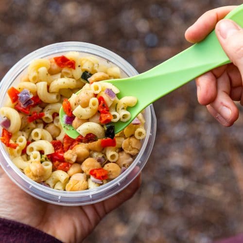 Megan holding a plastic container full of pasta salad. She's picking up a spoonful.