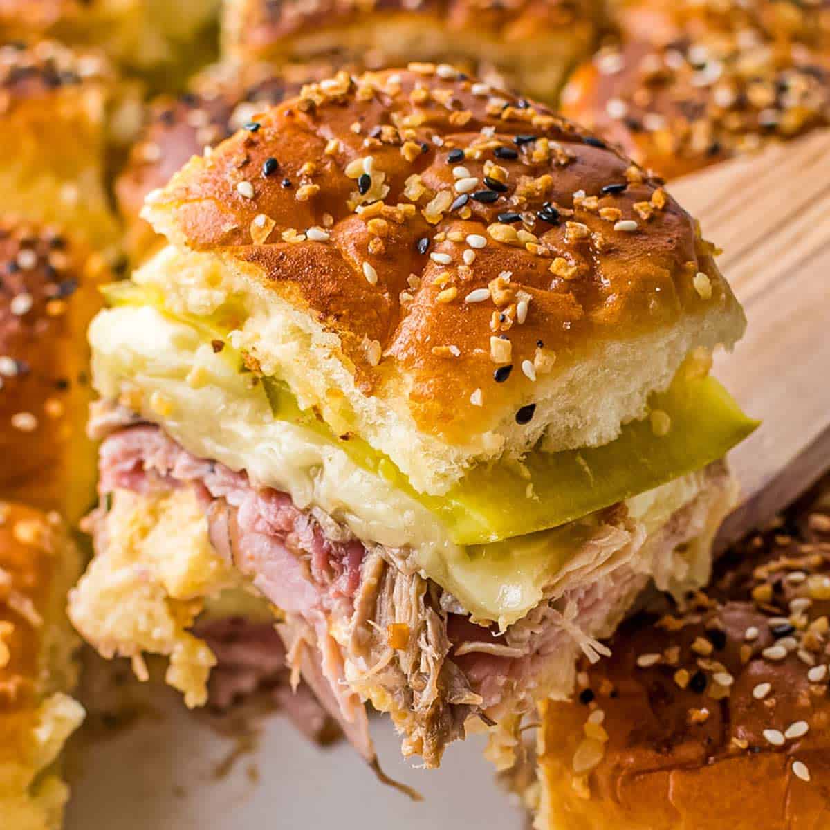 A close-up view of a Cuban sandwich with pulled pork, melted cheese, pickles and sesame seeds on the bun.