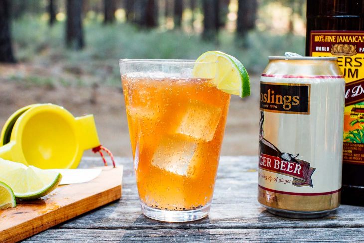 Dark and stormy in a clear glass. A bottle of rum and can of ginger beer are in frame.