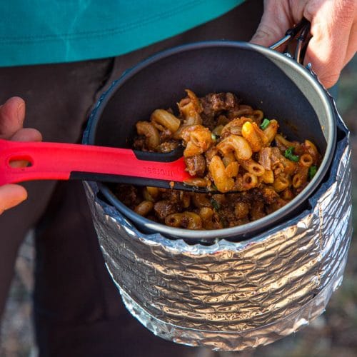 Megan holding a pot and using a spoon to scoop up chili mac.