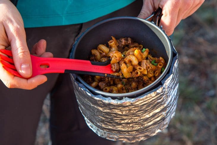 Megan holding a pot and using a spoon to scoop up chili mac.