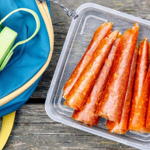 Fruit leathers rolled up in a tupperware on a wooden surface.