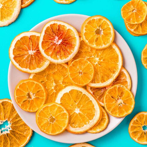 Dried orange slices on a plate surrounded by dehydrated orange slices.