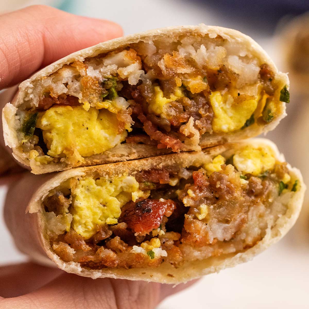 Close-up image displays a breakfast burrito sliced in half, revealing interiors of scrambled eggs, sausage, and spinach wrapped in a grilled tortilla.