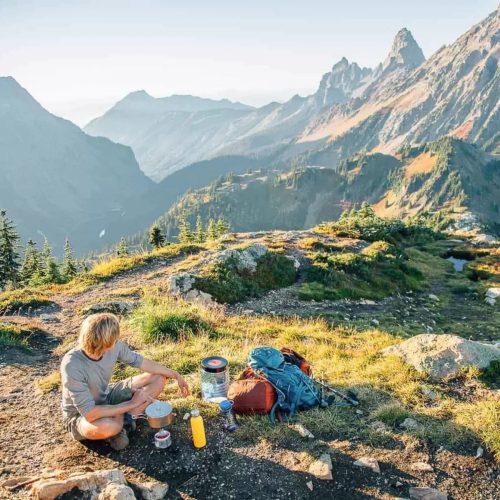 Michael sitting with his backpacking cooking kit and the Cascade mountains in the background