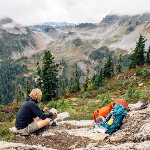 Man cooking a backpacking meal with mountains in the background.