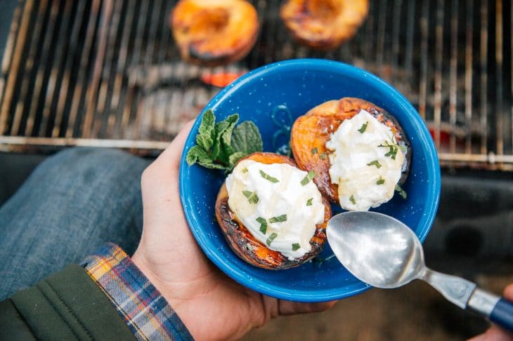 Two grilled peaches topped with yogurt in a blue bowl