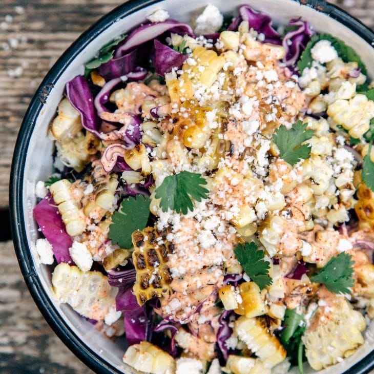 A bowl of grilled corn kernels, crumpled cheese, cilantro, and shredded red cabbage.