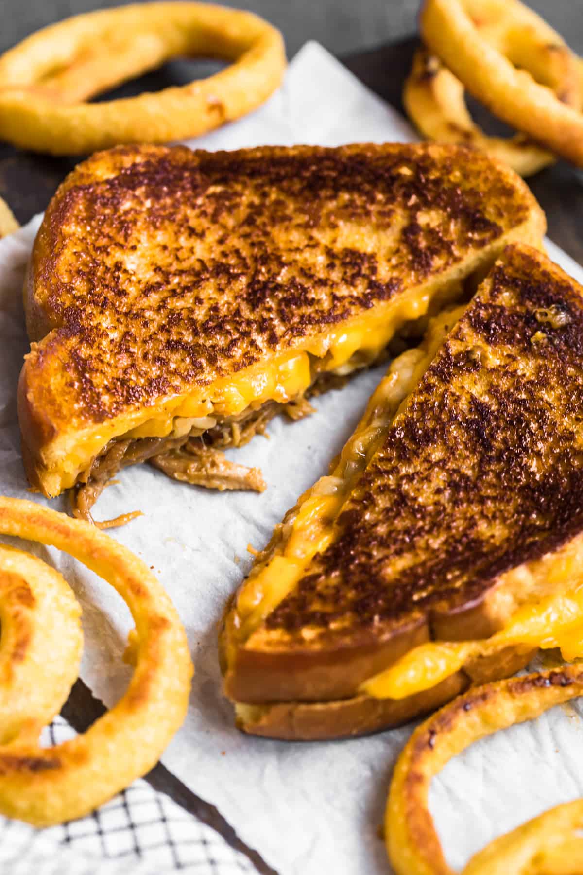 A grilled cheese sandwich, cut diagonally with oozing melted cheese, rests on a napkin alongside crispy onion rings.