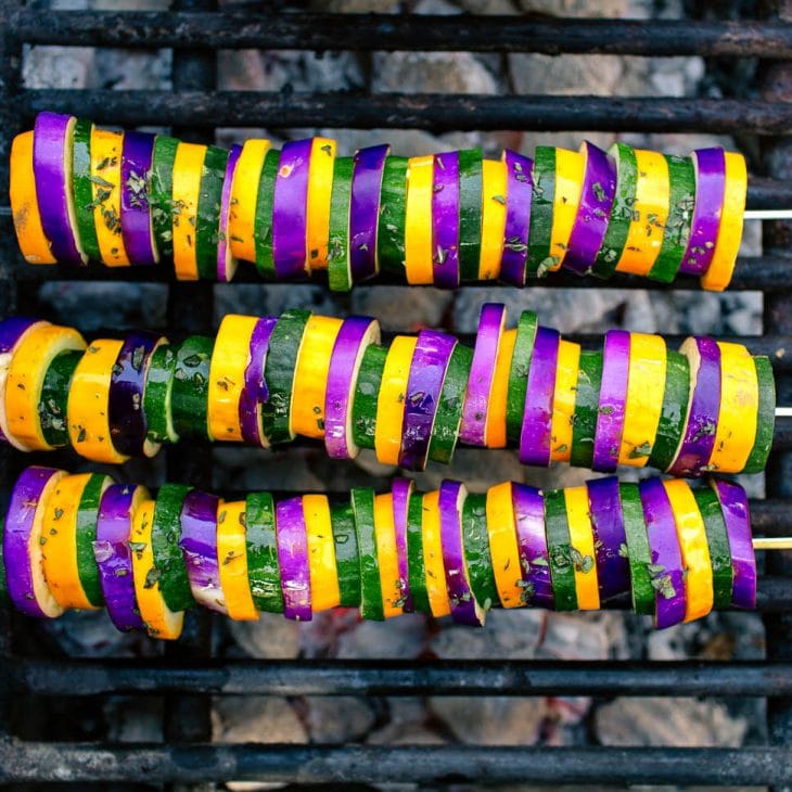 Three kabobs with sliced eggplant, zucchini, and yellow squash on a grill