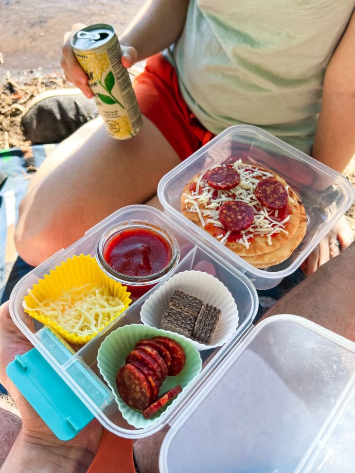 Megan sitting on a picnic blanket and Michael is holding a snack box on his lap