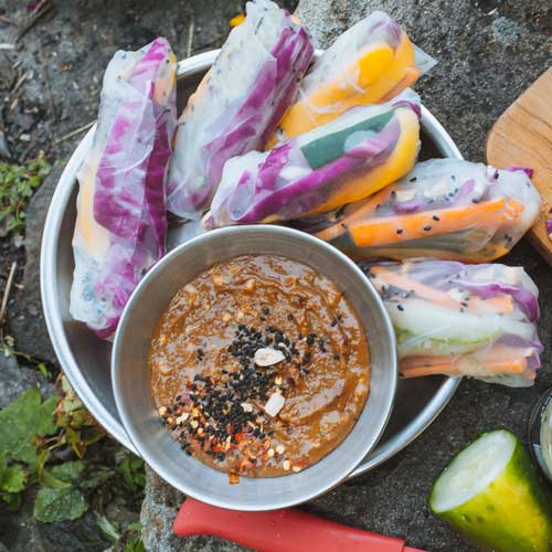 Summer rolls on a plate next to a bowl of almond butter satay sauce