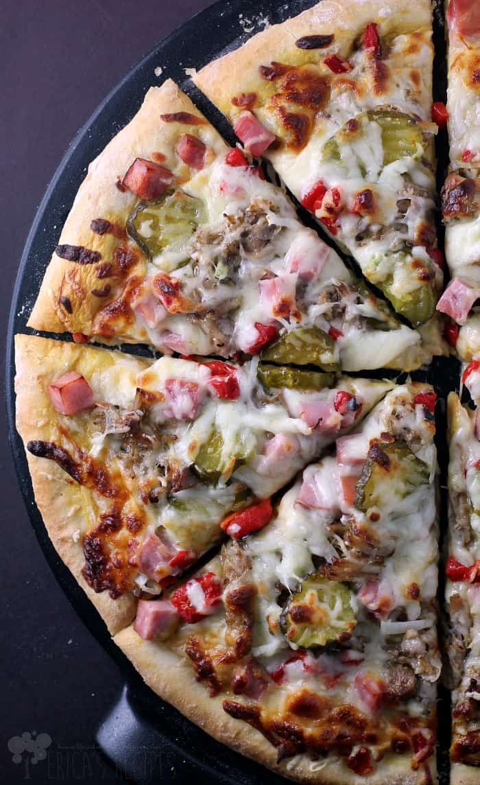 A large pizza topped with melted cheese, sausage, peppers, and onions is portioned into eight slices on a black tray.