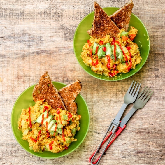 Two plates of scrambled eggs topped with fresh herbs and served with crispy toast, ready for a delicious breakfast on a rustic wooden table.